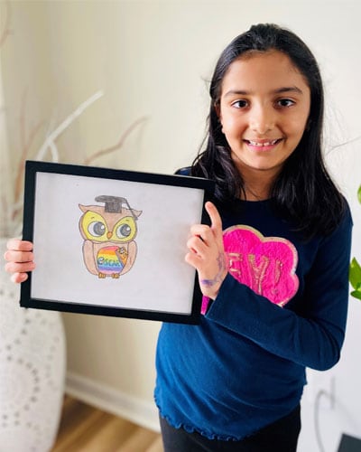 Image of a Connections Academy student in a dark blue shirt with a pink graphic element smiling holding up a drawing of an owl. 