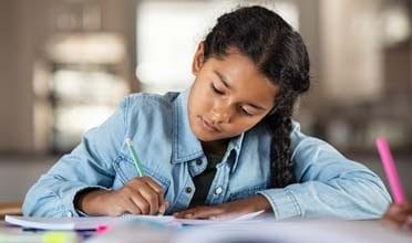 Image of a young girl in a denim shirt writing on a piece of paper. 