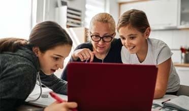 Image of a learning coach with her two young daughters looking at a laptop during an online class for Connections Academy. 