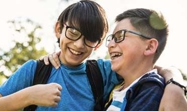 Image of two young male students smiling and laughing about something funny, both are wearing blue shirts. 