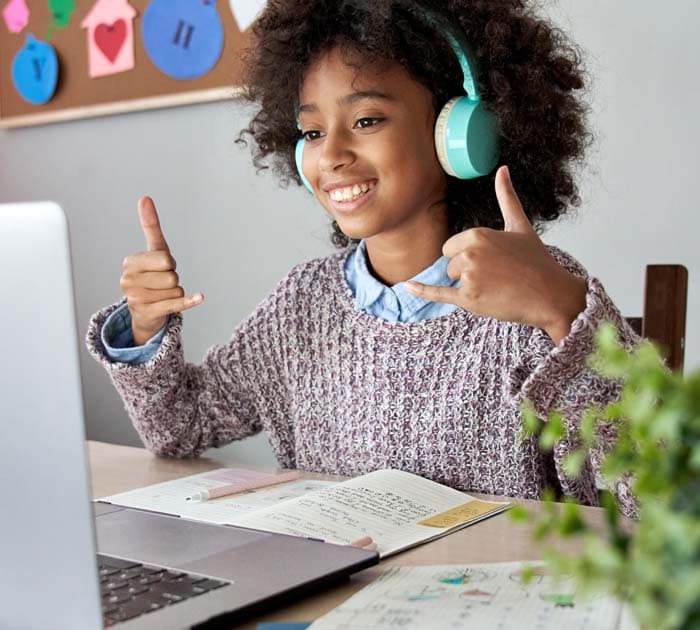 A smiling young girl sitting in front of a laptop with headphones on