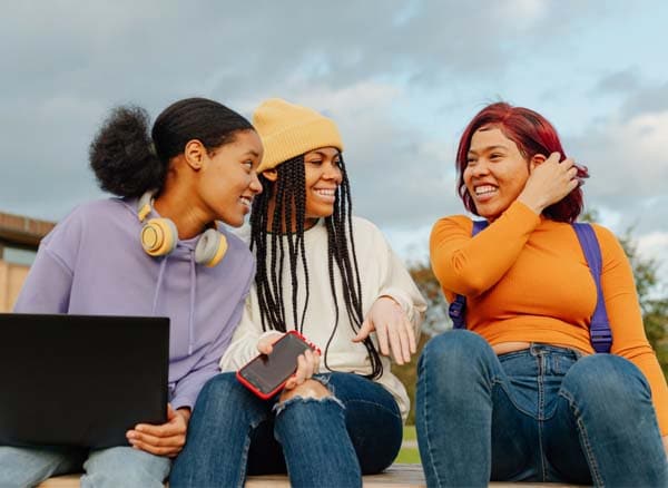 Three girls socializing while working on a laptop outside